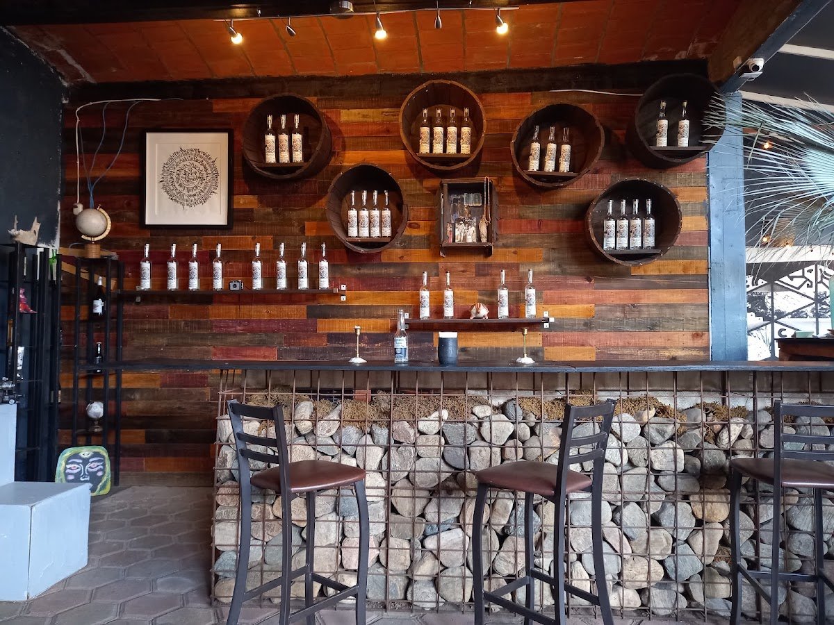 Barra con botellas exhibidas sobre una pared de madera y un frente de piedra.