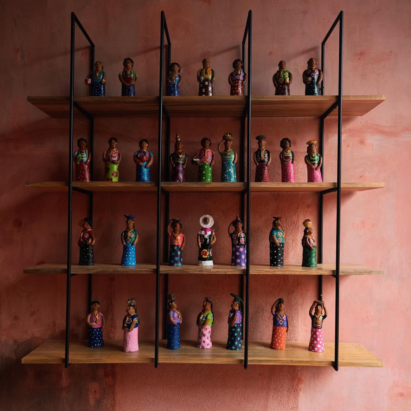 Figuras artesanales con vestimenta colorida alineadas en repisas sobre un muro color arcilla.